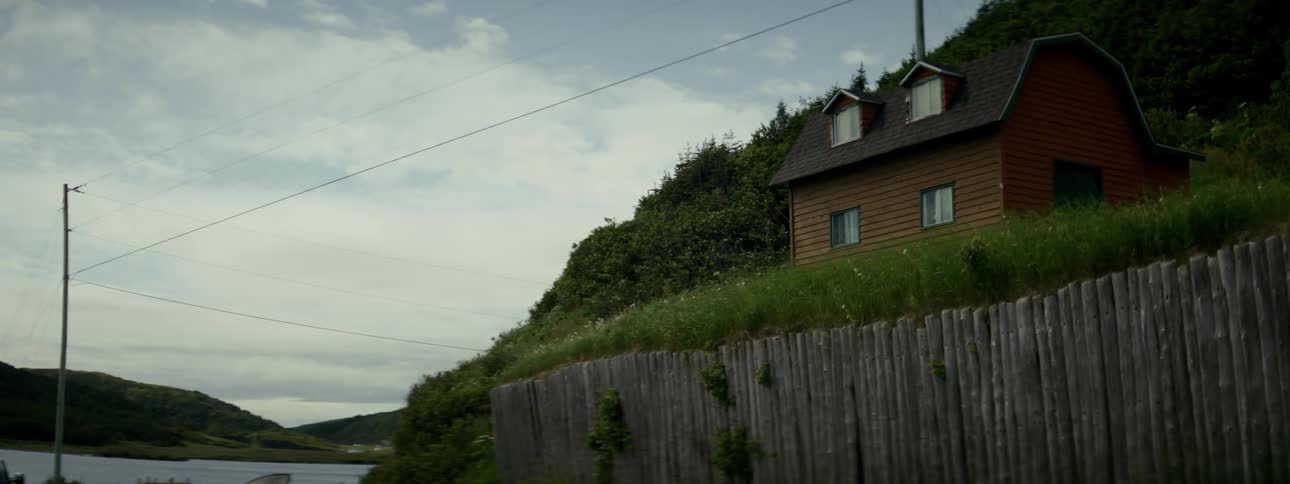 A small house sits on a plain on a hill near a lake