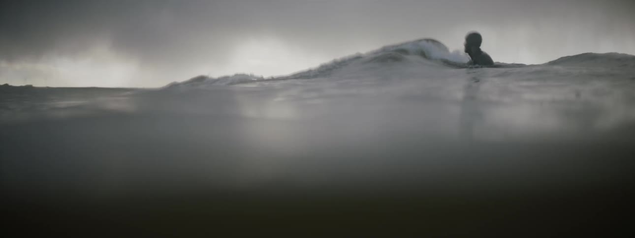 A surfer catches a wave while another floats nearby