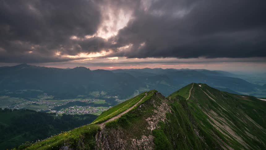 A large mountain covered with grass and a sky with an ash cloud it is getting late and the sky is setting