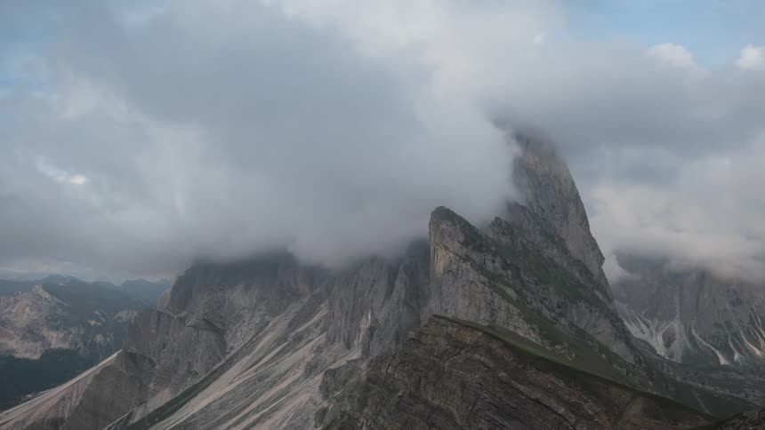 Mountainous landscape with a prominent peak under a cloudy sky with clouds passing by
