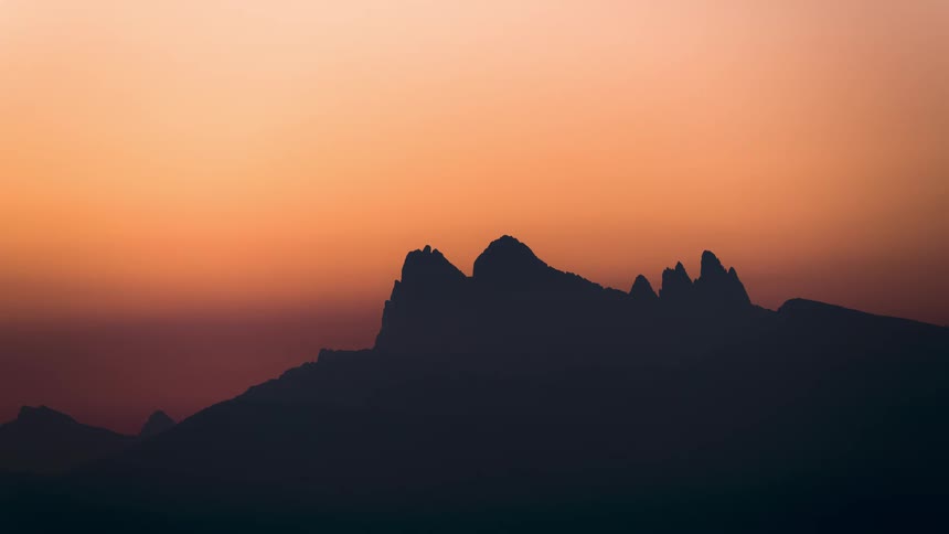 A silhouette of a dark mountain in contrast to an orange sky that is dusk