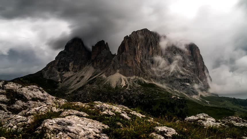 Clouds flow across mountain cliff standing on stony terrain