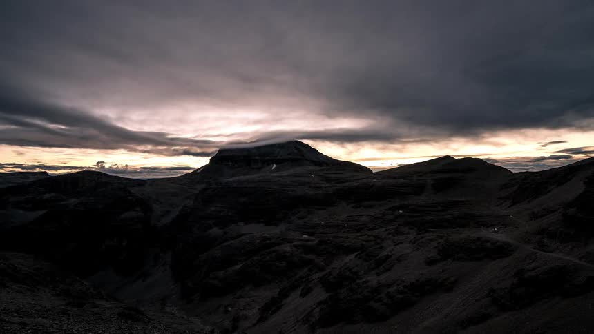 A mountainous region at night and it is becoming daytime and several clouds take over the environment