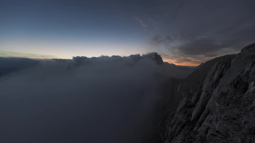 Time lapse of clouds rolling over steep mountain peaks from night to dawn