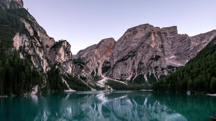 A landscape of a lake and behind it there is a big mountain and there is a small boat moored on the lake moving with the tide