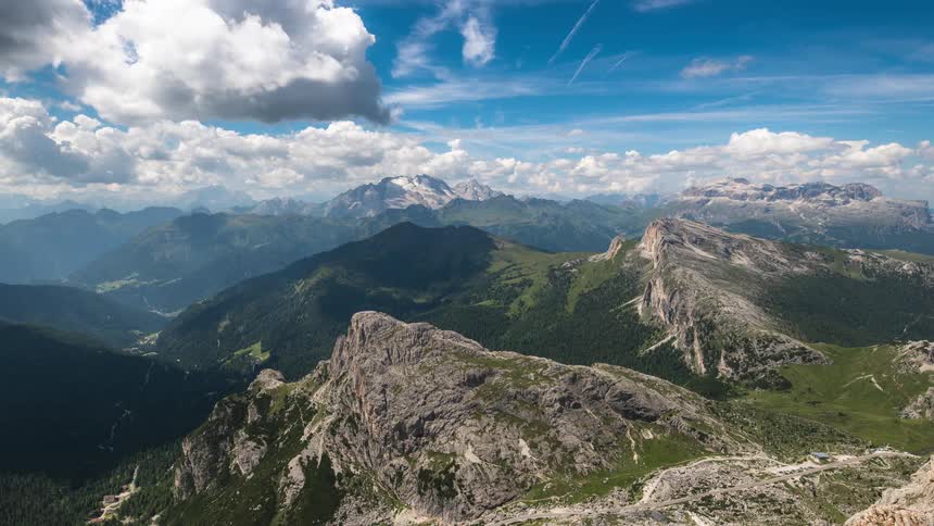 Clouds scoot across the sky over a large mountain range near a rural area