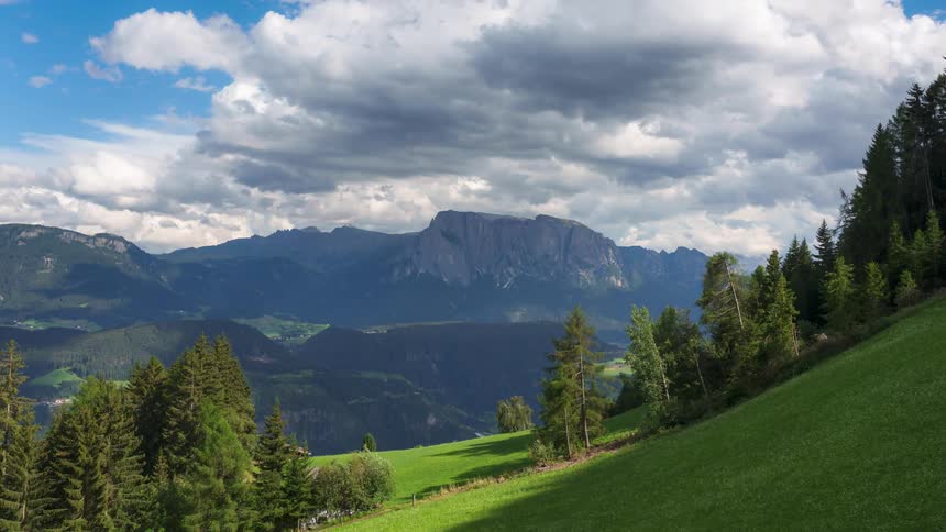 Clouds move over mountains and a valley near a house in a rural area