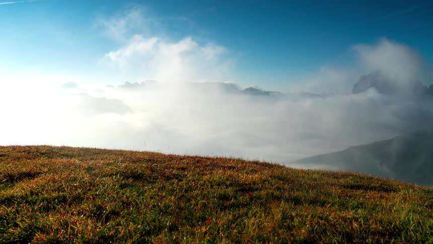 Time lapse of a grassy hill in front of a landscape of clouds rolling over the mountains