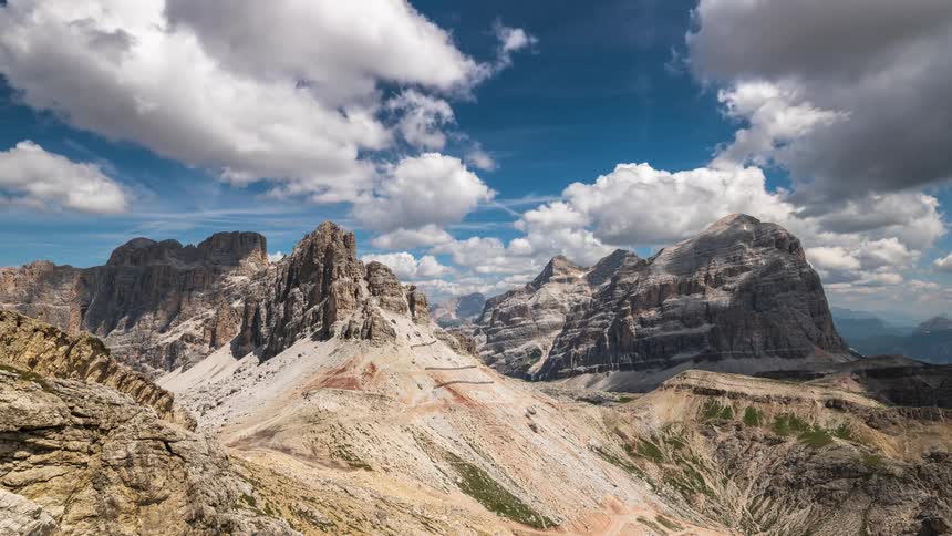 A mountain range with rocky mountains illuminated by sunlight and there are many white clouds moving in the sky