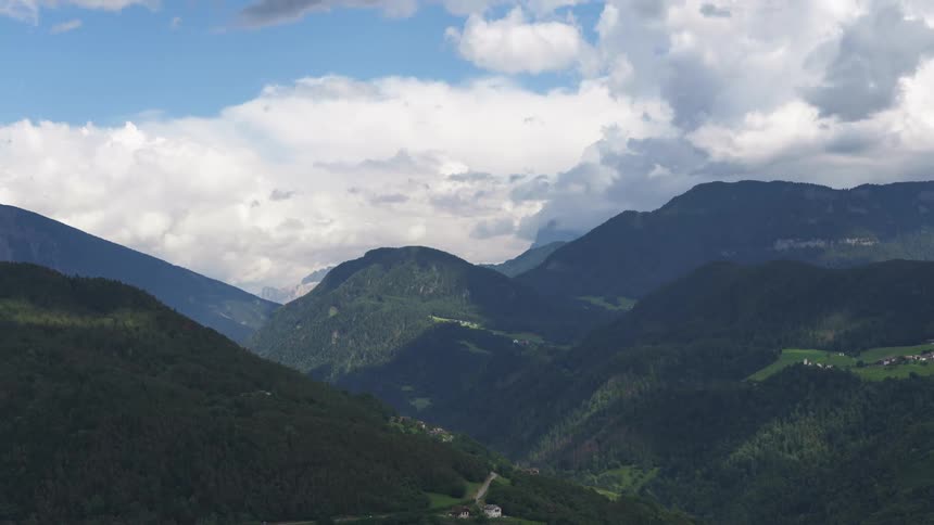 A valley between mountains covered with trees with green leaves and white clouds passing quickly in the sky