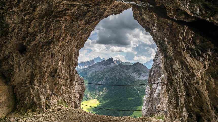 Cave mouth overlooks forest valley at foot of mountain range