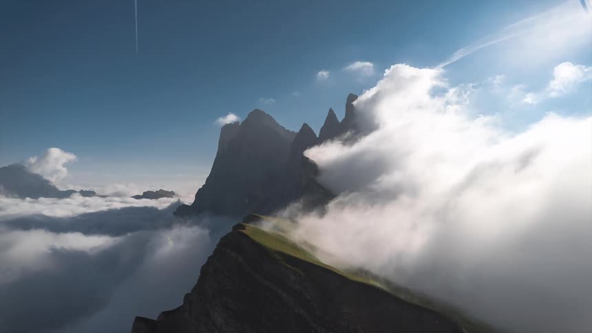 Time lapse of clouds forming and rolling against sharp mountain tops under a clear blue sky