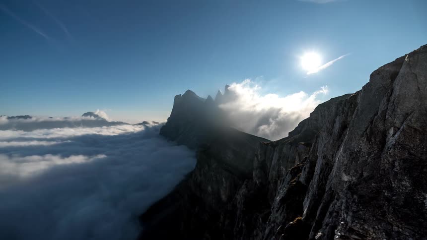 Scenery with rocky mountains at cloud level and the strong sun on the horizon