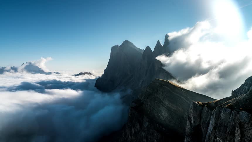 Towering mountain range with sharp peaks that emerge above a sea of clouds under a clear blue sky