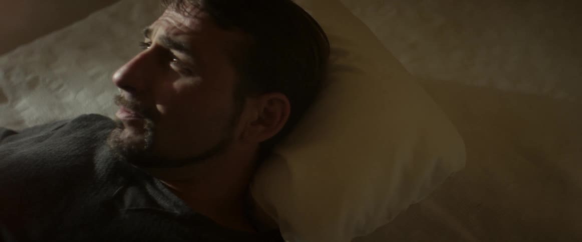 A man lying on a bed smoking  and looking worried