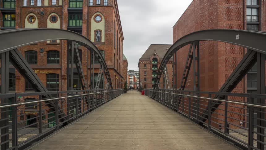 People walk on a bridge over a street in a city as traffic passes by