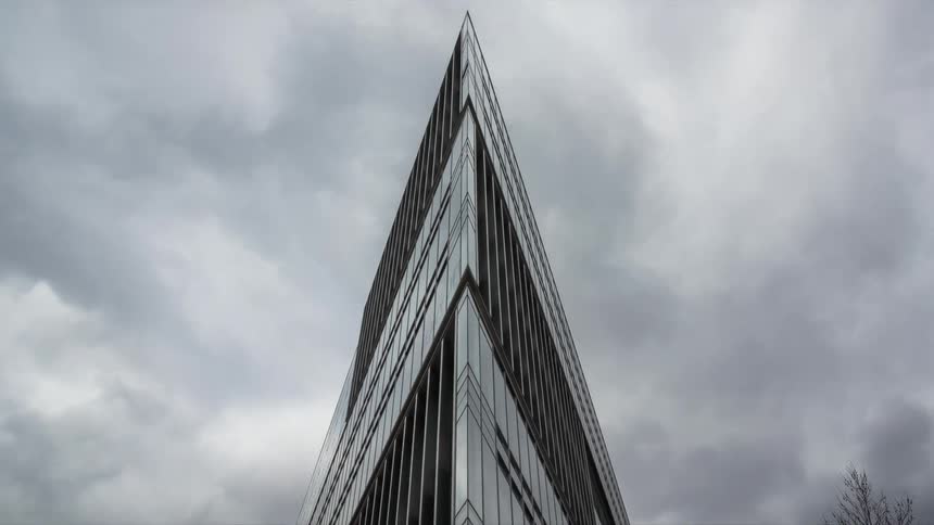 Highrise modern building with a sharp triangular facade pointing to the sky with cloudy clouds passing by