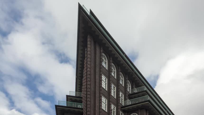 A triangularshaped residential building in contrast to the blue sky and several white clouds passing by