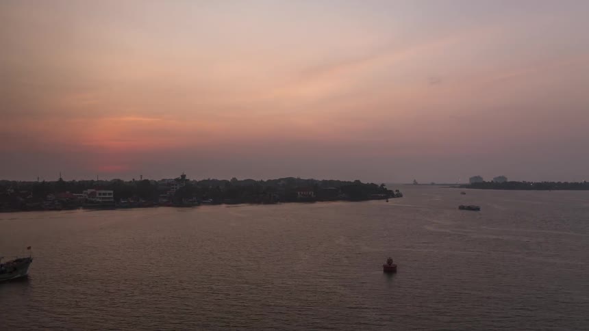 Sunset over a large river with the sun reflecting on the water and getting dark with some small boats sailing