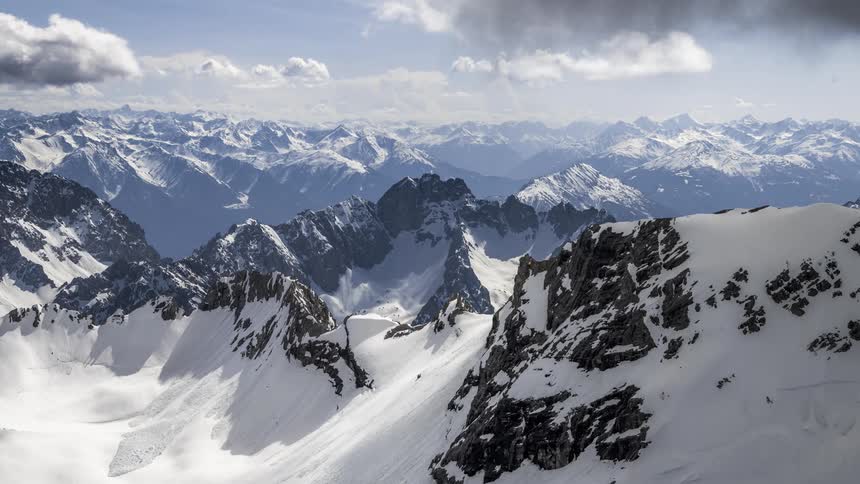 A mountain range covered in snow and several white clouds passing over them