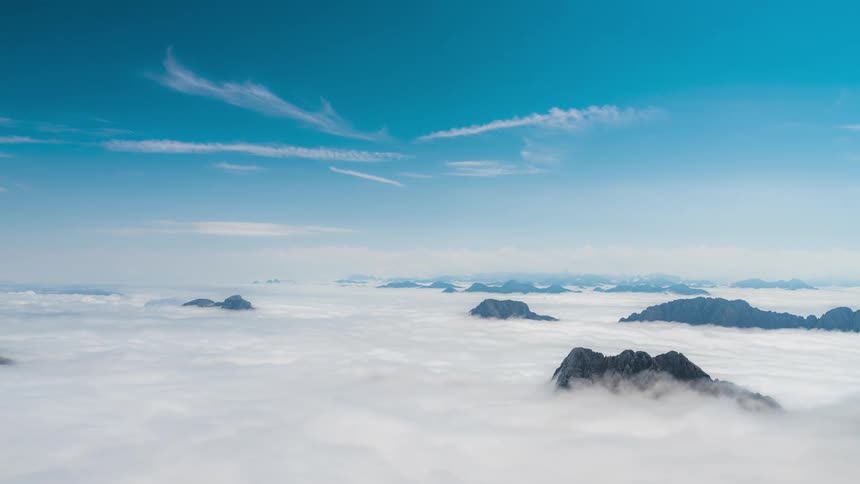 Sea of clouds passing over mountain peaks against a blue sky