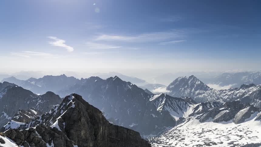 Wispy clouds pass over a snowy valley enclosed between the rough mountains ofa mountain range in winter