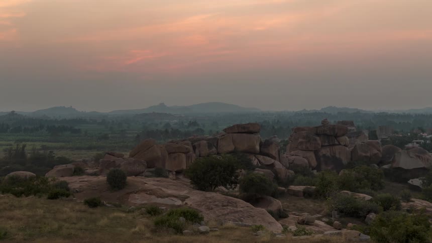 Boulders form natural wall on grassy plain as sun sets over mountains on the horizon