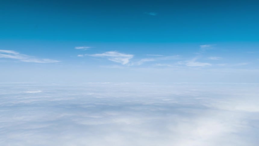 An aerial view above the clouds with them forming a sea of white clouds below and the clear blue sky above