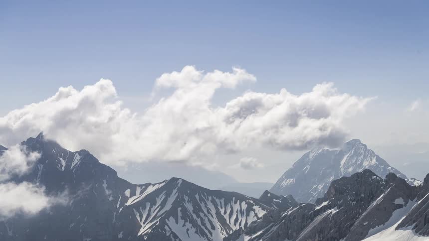 Large clouds roil over a snowy mountain range