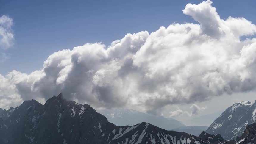 Mountain range with snowcapped peaks under a clear blue sky and white clouds