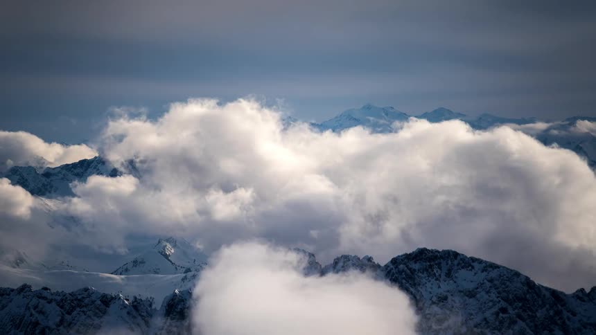 White clouds flow past snowy mountains on an overcast winter day