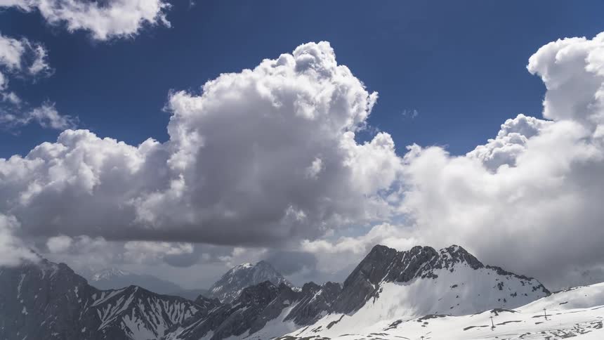 Dense white clouds passing quickly over a mountain range with snowy mountains