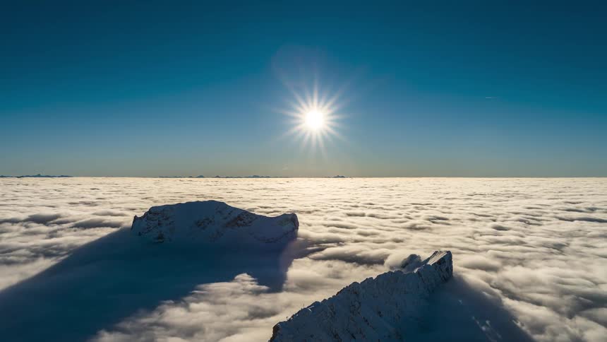 The sun shines bright on the clouds and mountain peak