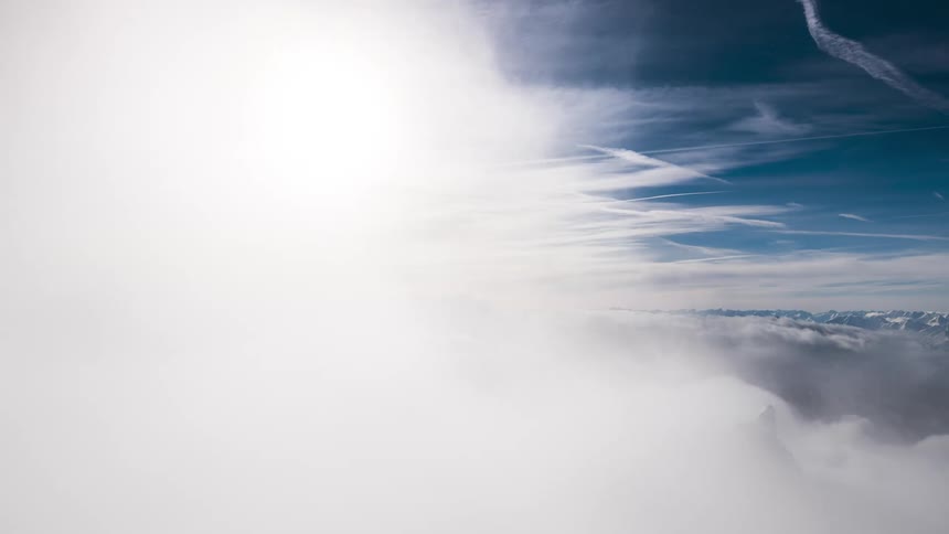 Clouds flow across mountainous terrain under a glaring sun