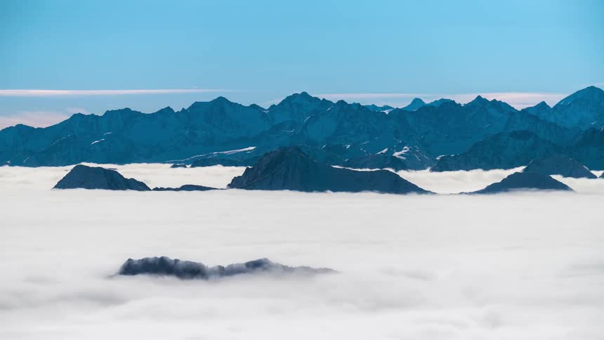Mountain range with jagged peaks rising above a dense layer of clouds under a clear blue sky