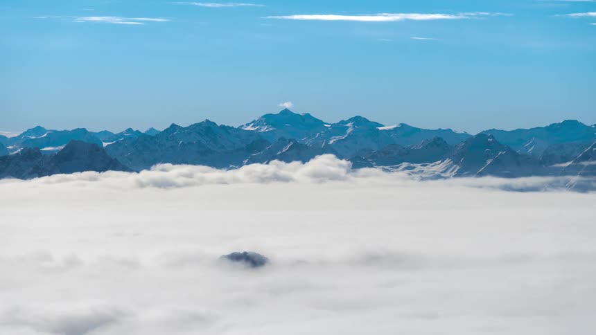Mountain range with snowcapped peaks that rise above a vast sea of clouds