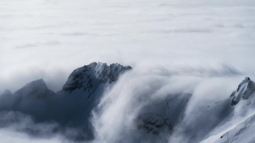 Sea of clouds passing through snowy mountain peaks