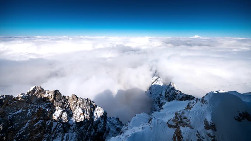 Dense clouds pass tall snow covered mountain peaks