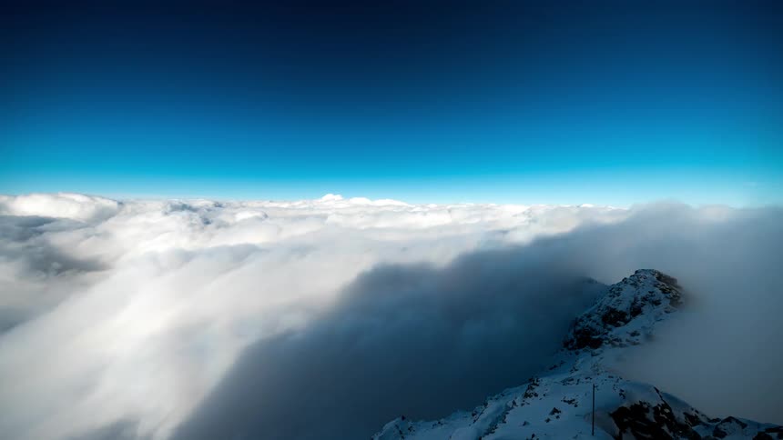 Snowcovered mountain peaks with a sea of clouds passing by