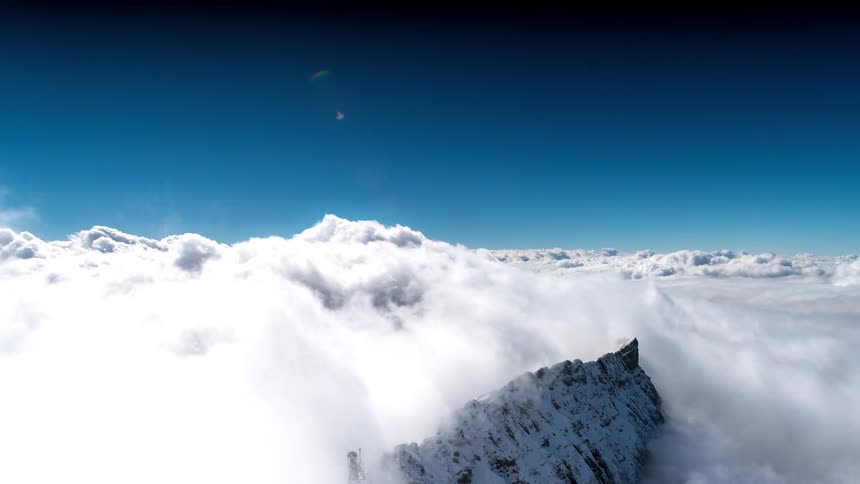 A view of a snowy mountain peak in an environment covered in dense white clouds