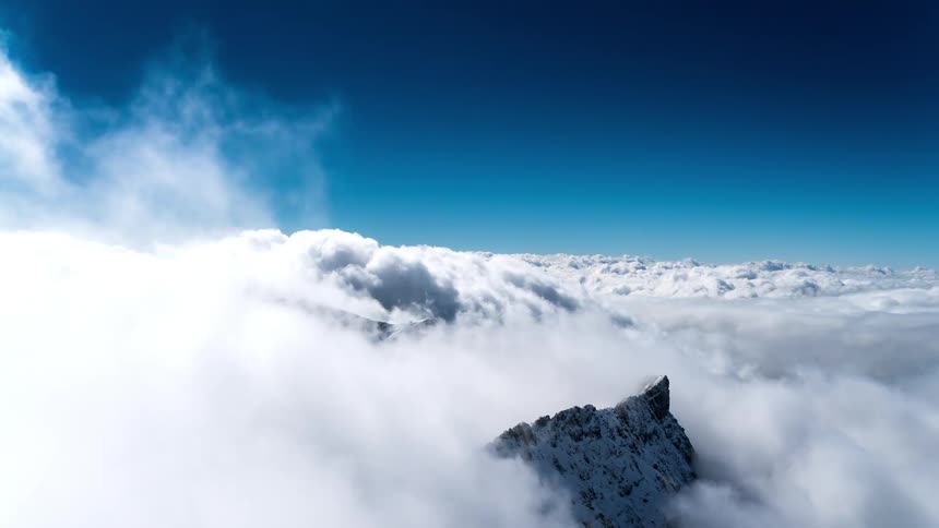 A very high view from above of ice mountains to a sea of white clouds and a blue sky above