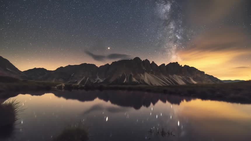 A night sky with stars the milky way galaxy and mountains reflected in a calm body of water