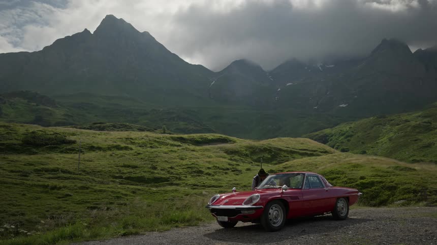 A man is leaning on a car parked by the mountains