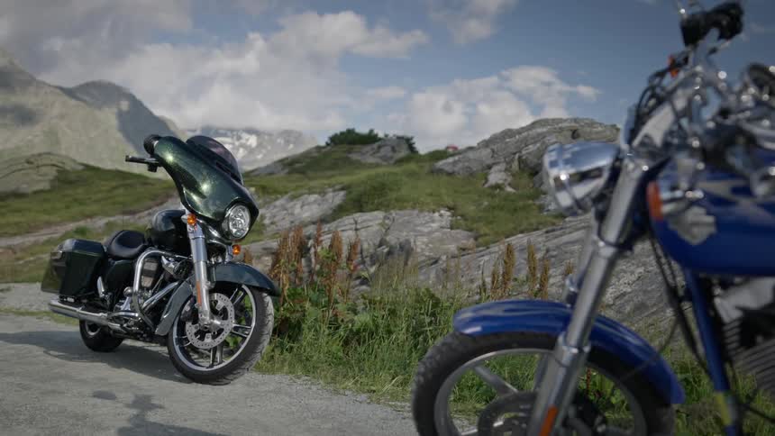 Brightening sunlight casts shadows under motorcycles parked on rural road through hilly terrain