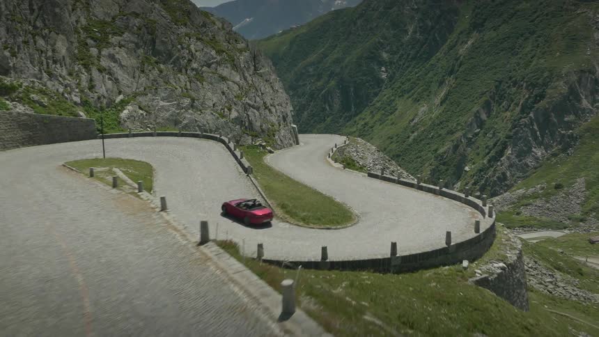 A red sports car driving on a spiral road that climbs a mountain