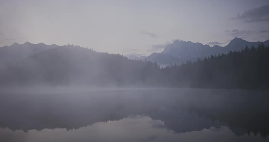 Fog obscures lake reflecting nearby forested mountains