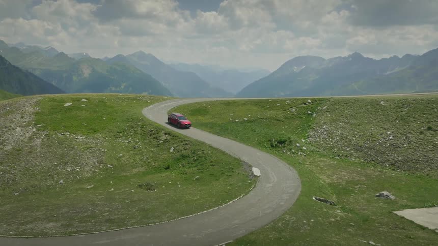 A car drives down a winding road a mountain range can be seen in the distance