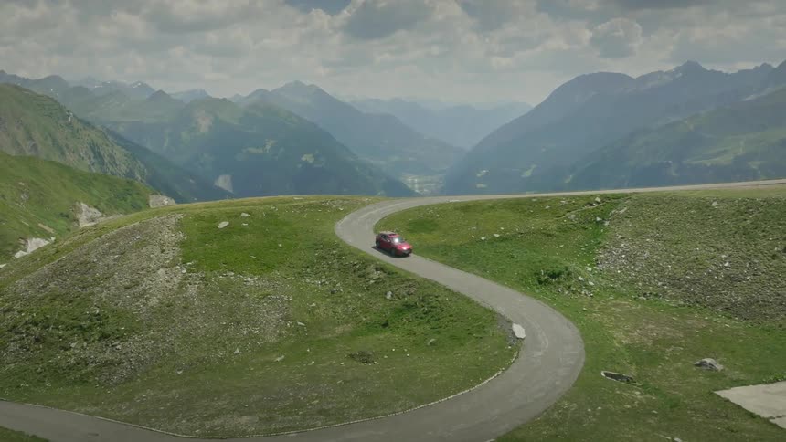 Red motor vehicle drives along road winding across mountain in mountainous terrain