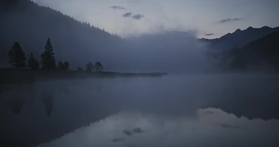 Clump of fog floats across the water bordering the mountains after dusk