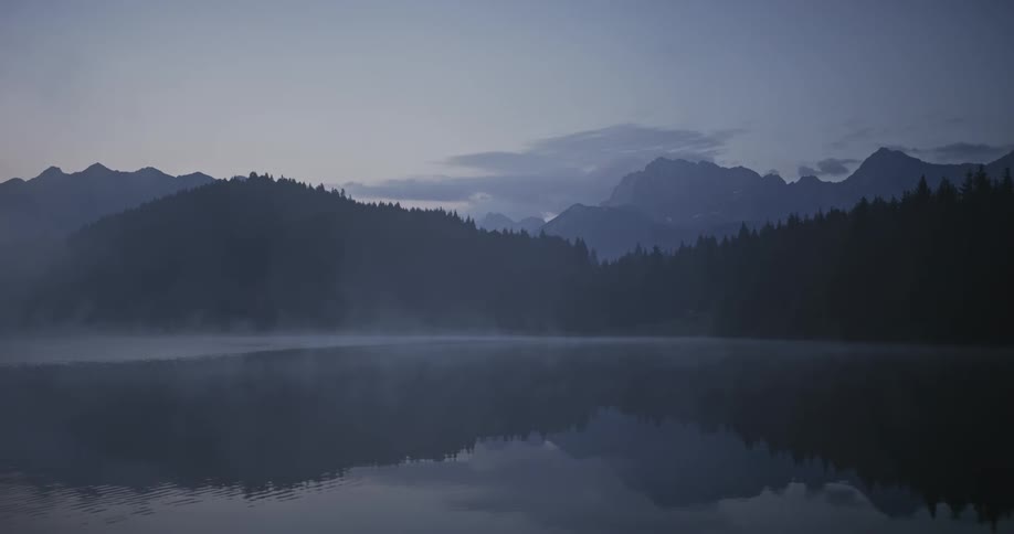 Gentle ripples move across a lake located near mountains and a forest